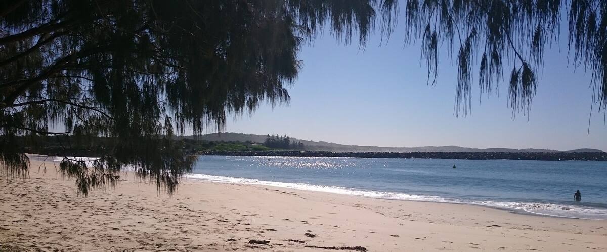A beach with clear water, sandy shore, and distant hills.