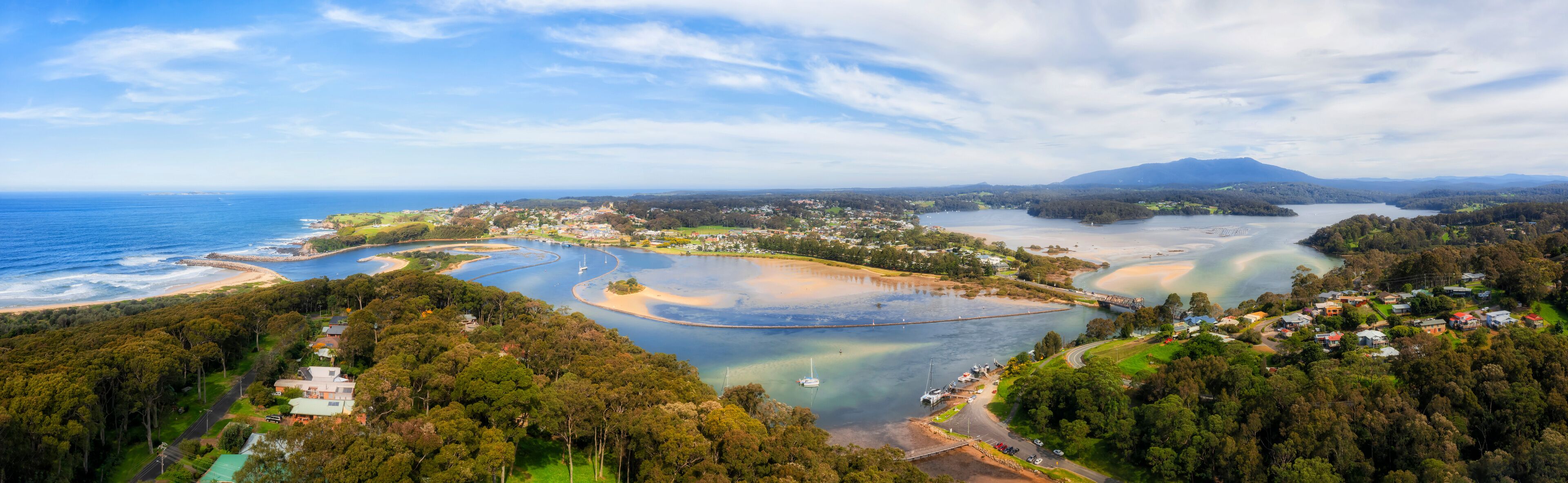 A coastal landscape with a bay, a bridge, and a mountain in the distance.
