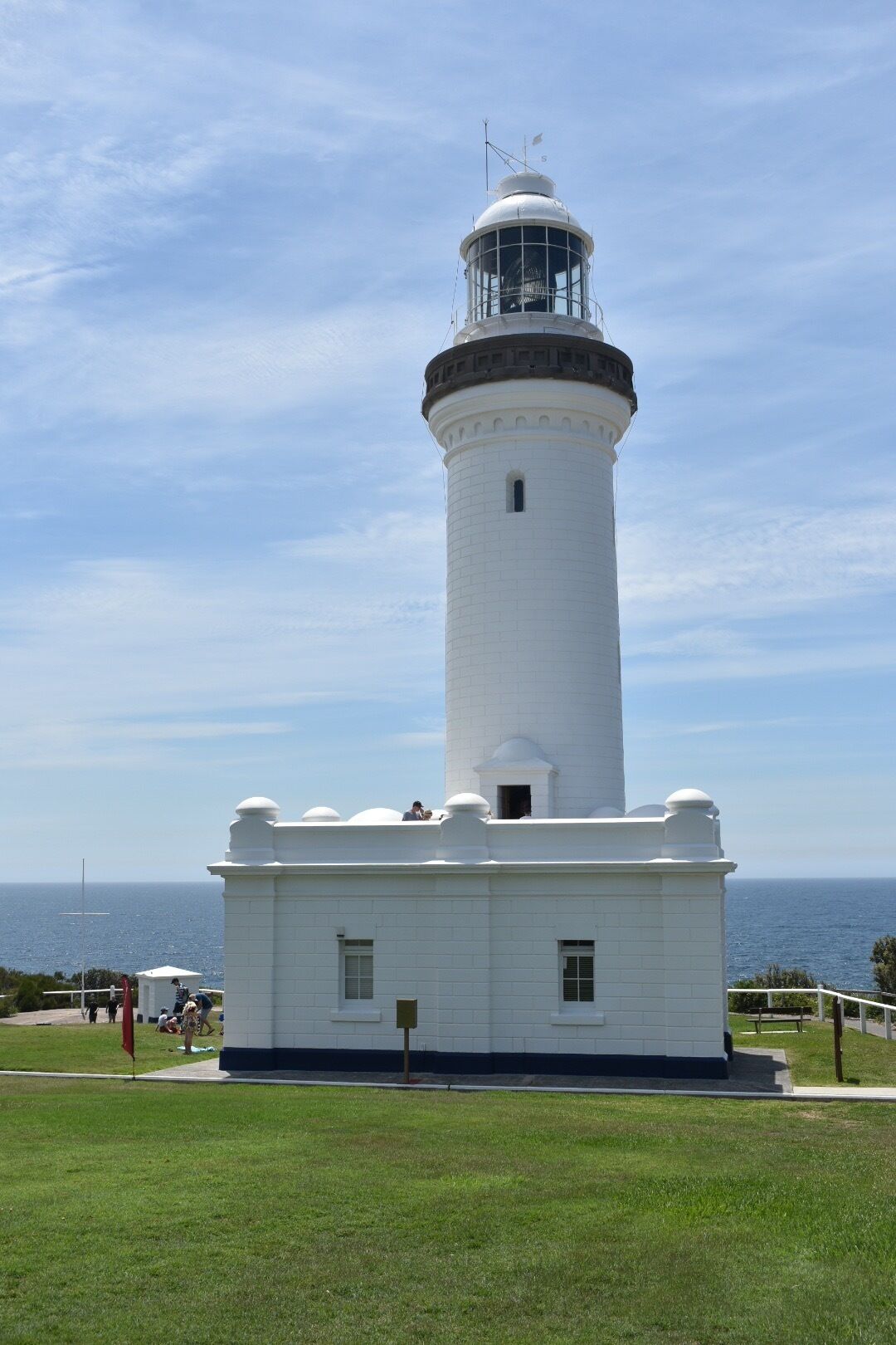 A white lighthouse with a black top, surrounded by a grassy area and a clear sky.