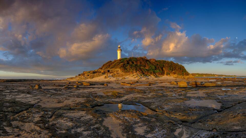 A rocky shoreline with a lighthouse on a small hill.