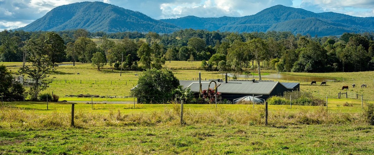 A rural landscape with a farm, grazing cattle, and a mountain range in the background.