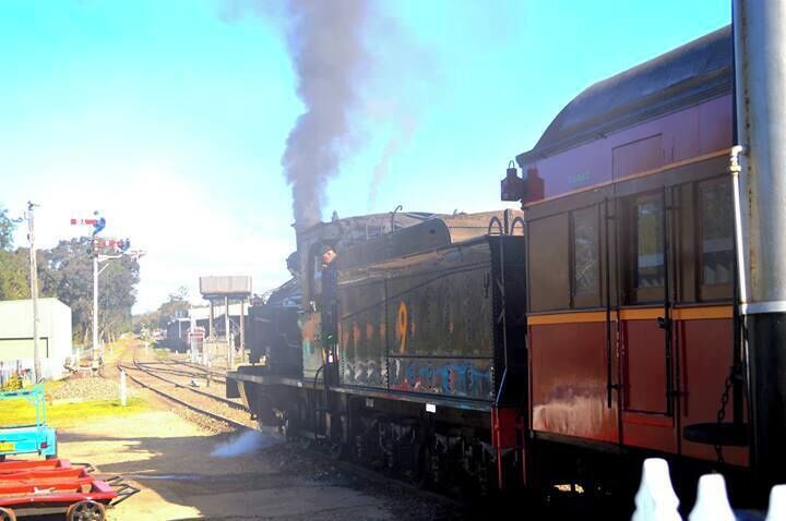 A steam locomotive with black smoke, a red and yellow passenger car, and railway tracks.