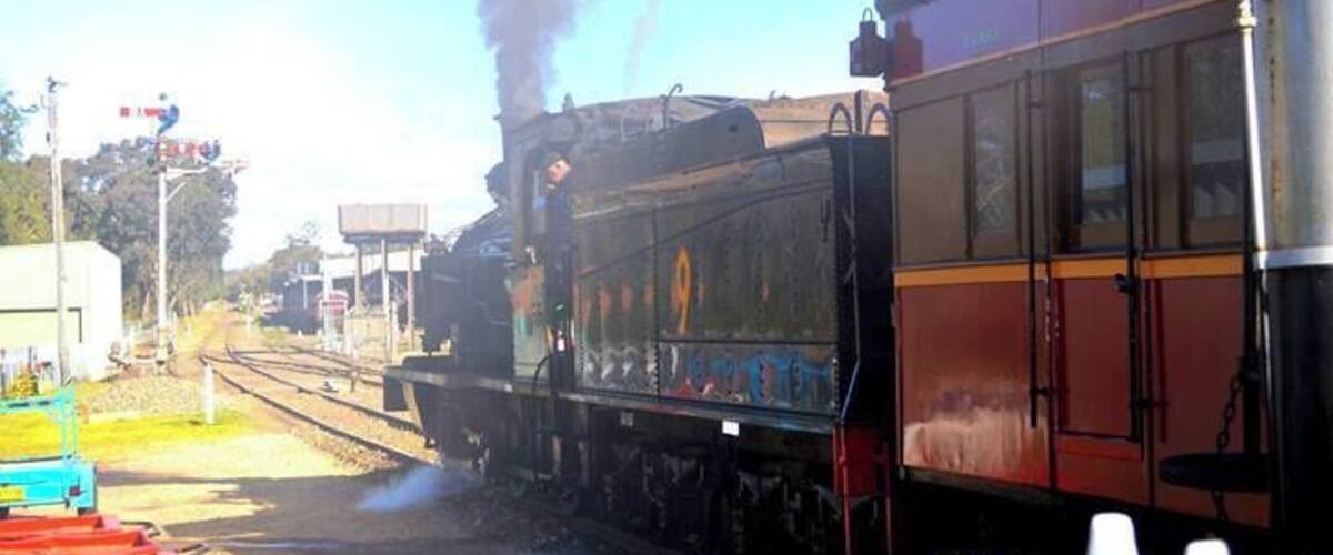 A steam locomotive with black smoke, a red and yellow passenger car, and railway tracks.