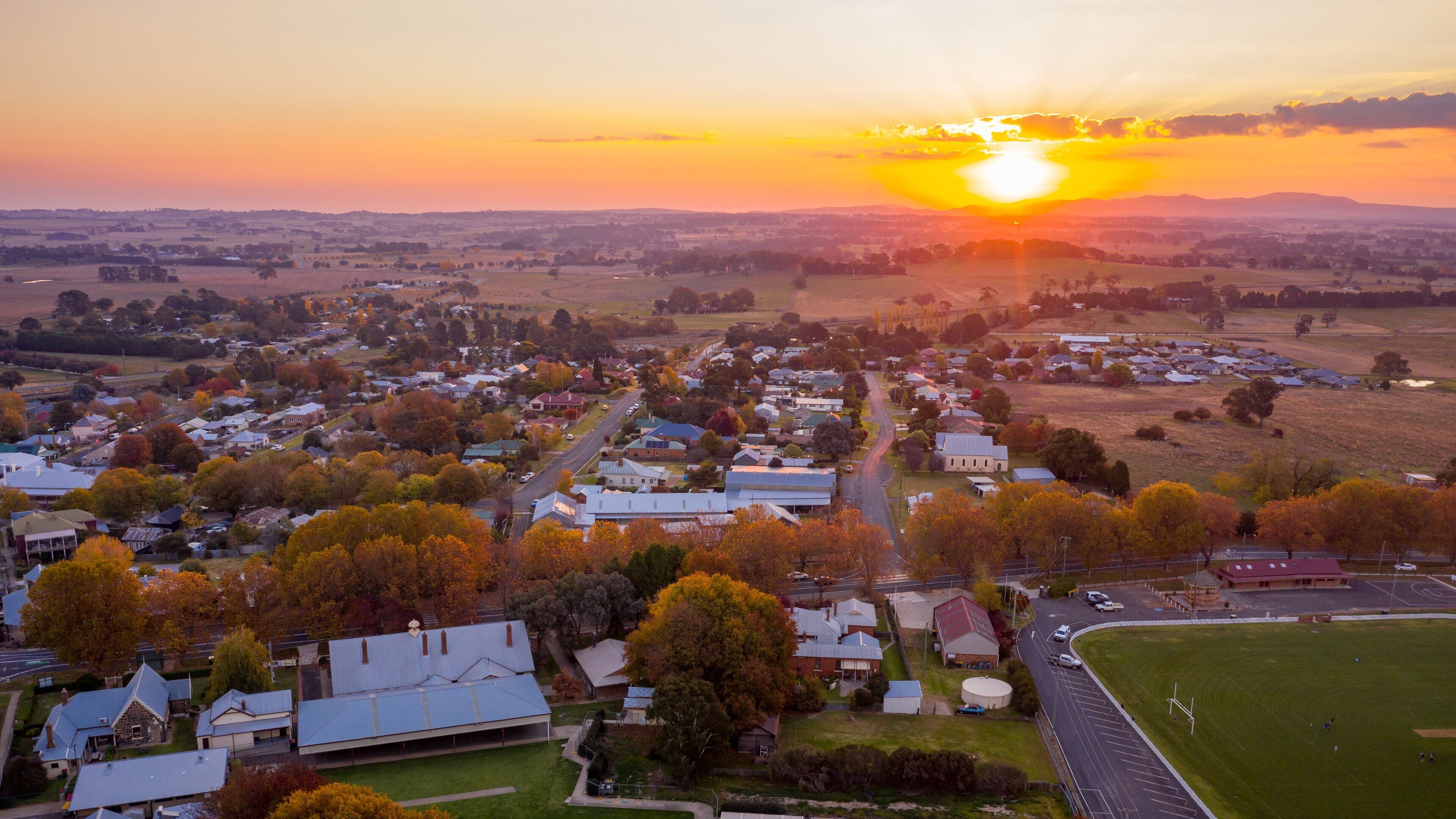 A rural town at sunset with houses, roads, and fields.