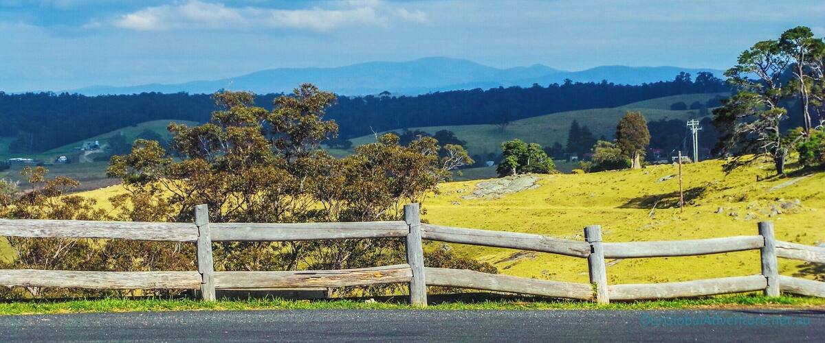 A wooden fence, rolling hills, and distant mountains under a partly cloudy sky.