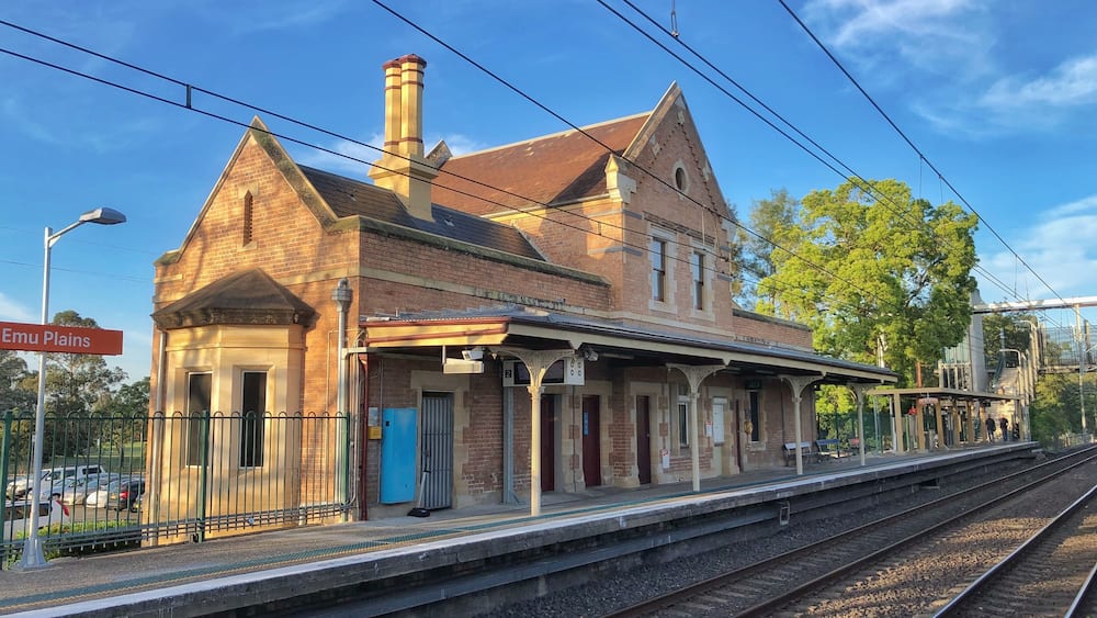 A historic train station with a brick building, a blue door, and tracks.