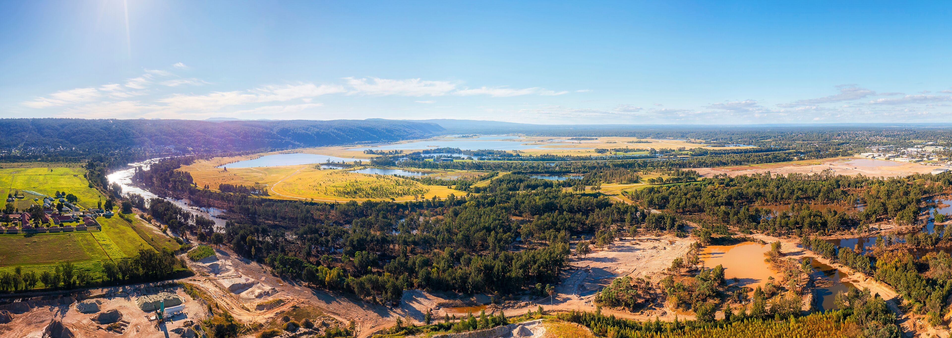 A river winding through a valley with a mix of forested areas and open fields, a small town, and a large body of water.