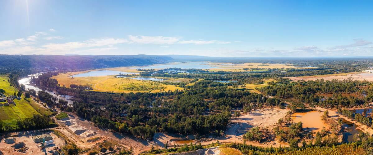 A river winding through a valley with a mix of forested areas and open fields, a small town, and a large body of water.