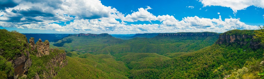 Un paisaje montañoso con densos bosques verdes y acantilados rocosos bajo un cielo parcialmente nublado.
