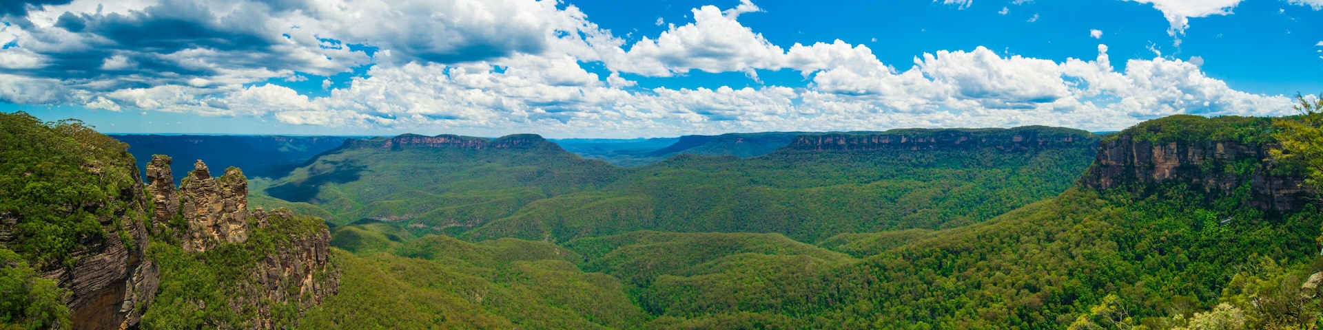 Un paisaje montañoso con densos bosques verdes y acantilados rocosos bajo un cielo parcialmente nublado.