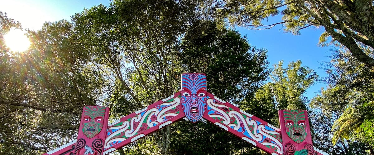 A traditional totem pole with intricate carvings and a backdrop of lush greenery and trees.