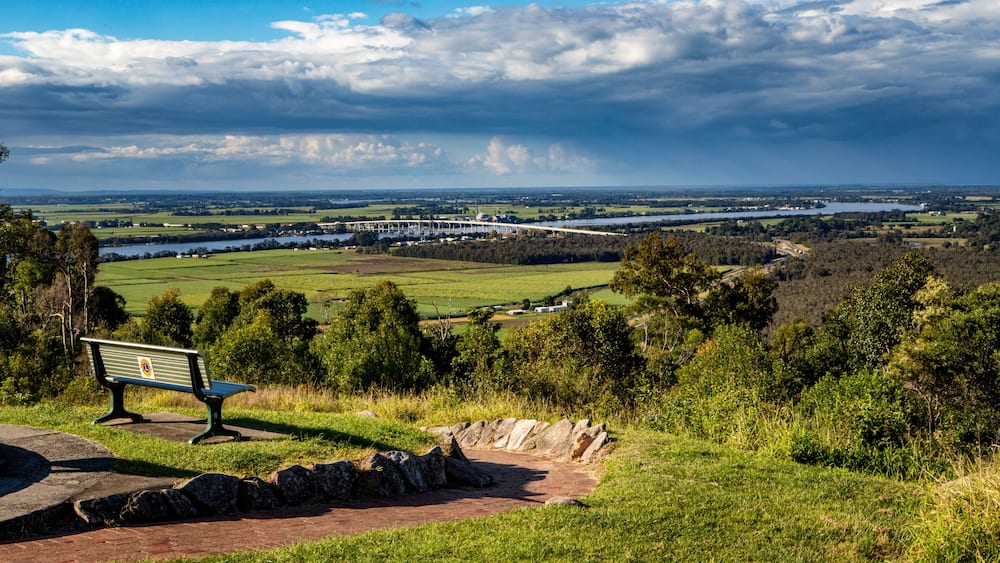 A bench overlooking a river, fields, and a bridge in the distance.