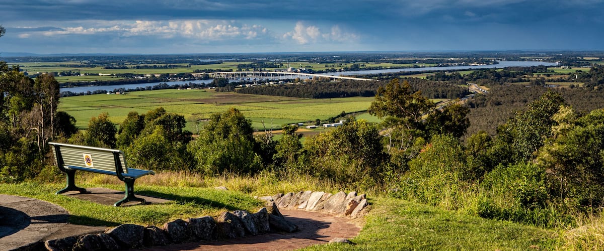 A bench overlooking a river, fields, and a bridge in the distance.