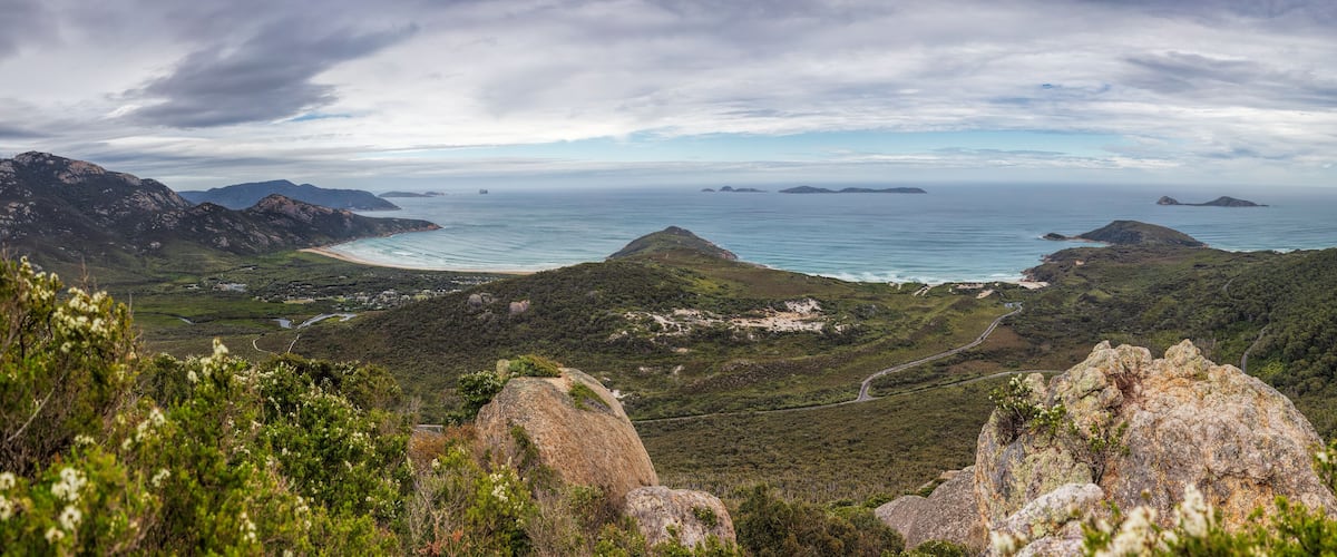 A coastal landscape with mountains, a beach, and a winding road.