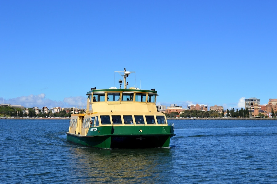 A green and yellow ferry named 'HINTER' on a body of water with a city skyline in the background.