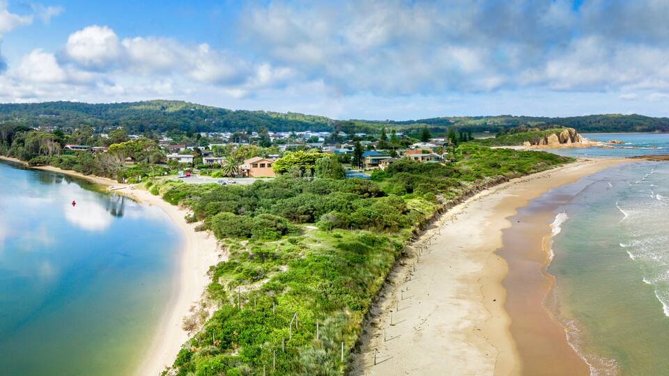 A coastal landscape with a beach, a river, and a town with houses and greenery.