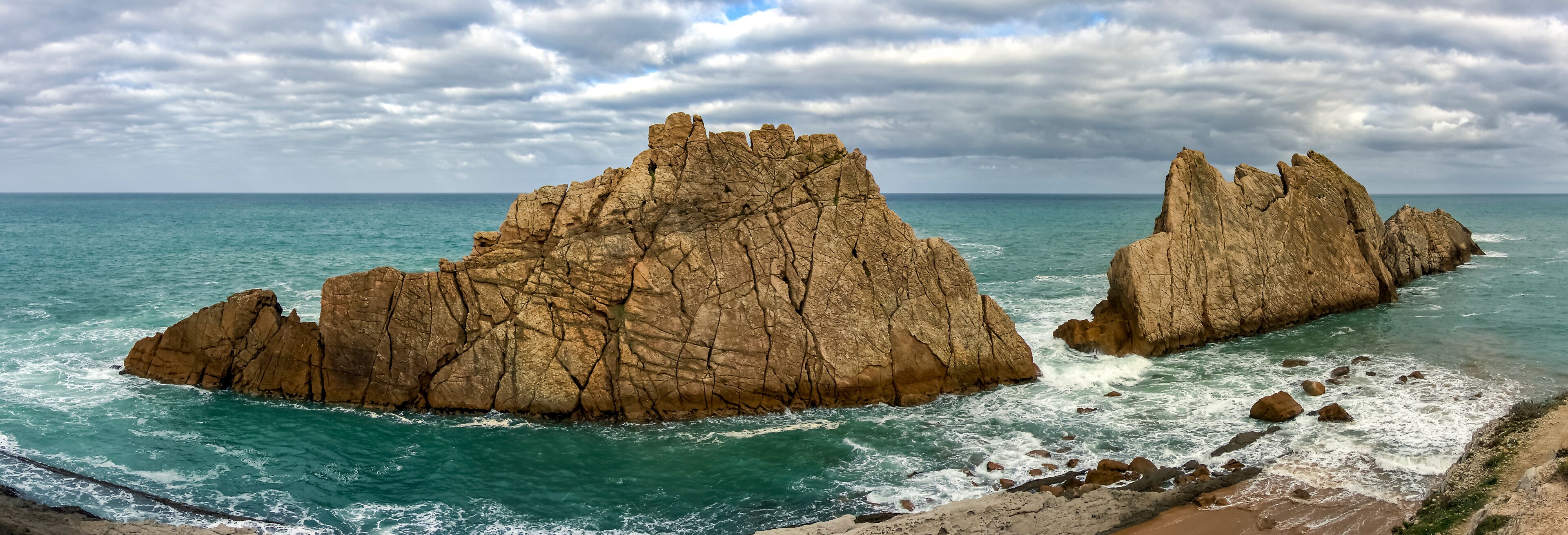 A coastal landscape with two prominent rock formations and a beach.