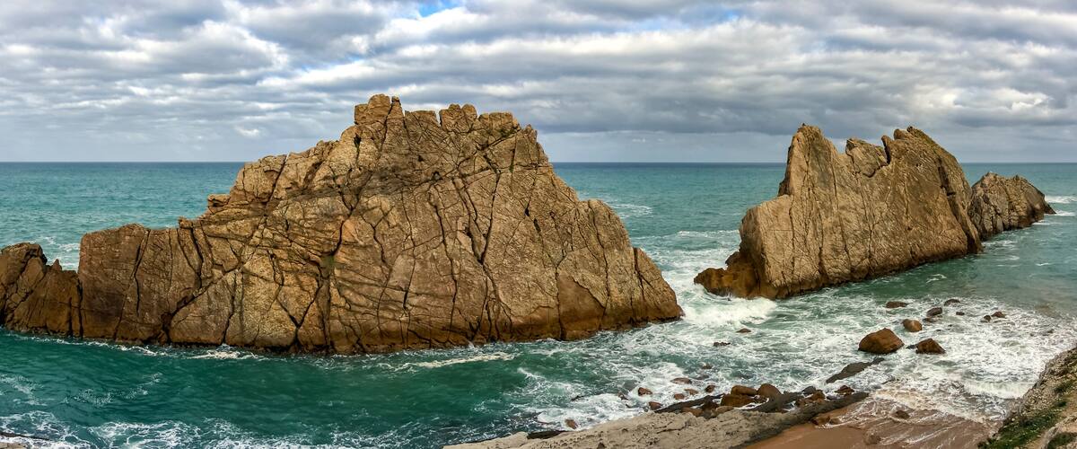 A coastal landscape with two prominent rock formations and a beach.
