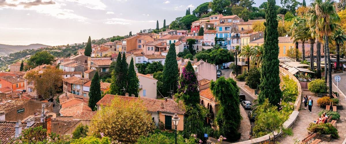 A hillside town with terracotta-roofed buildings, cypress trees, and a winding street.