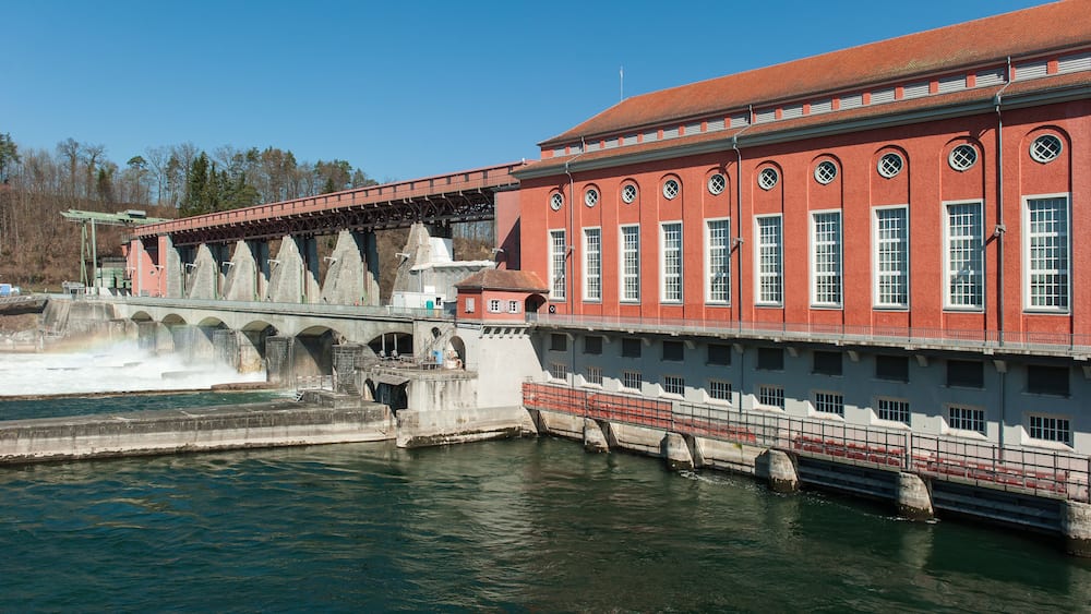 A large red brick building with arched windows and a bridge over a river.