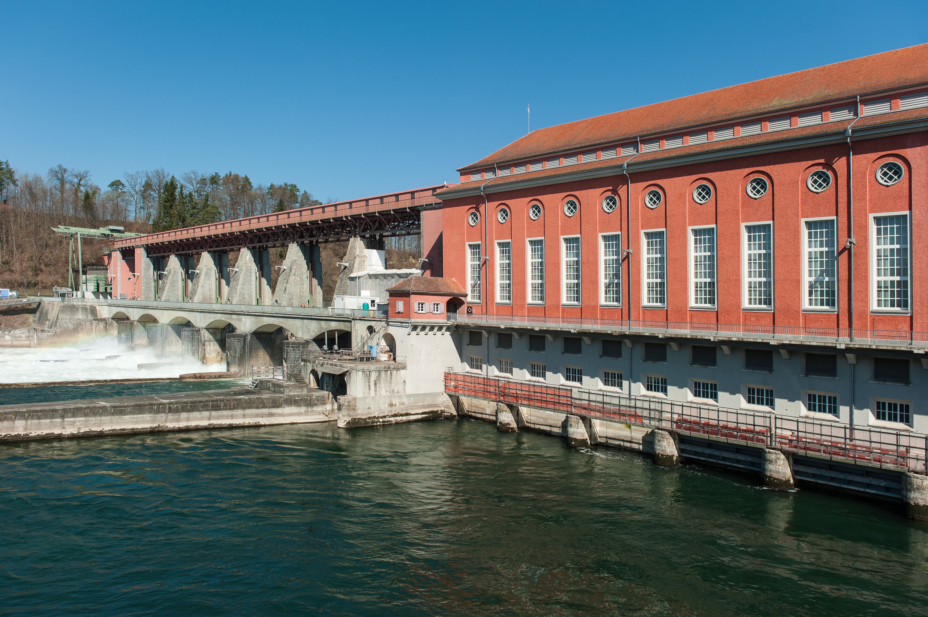 A large red brick building with arched windows and a bridge over a river.