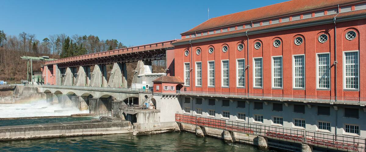 A large red brick building with arched windows and a bridge over a river.