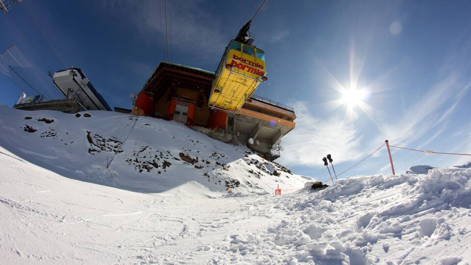 A ski lift with a yellow sign, a snowy mountain slope, and a clear blue sky.