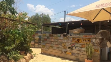 Un café situé au bord de la route, avec une enseigne indiquant différents numéros de téléphone et un panneau signalant la présence d’un train touristique.