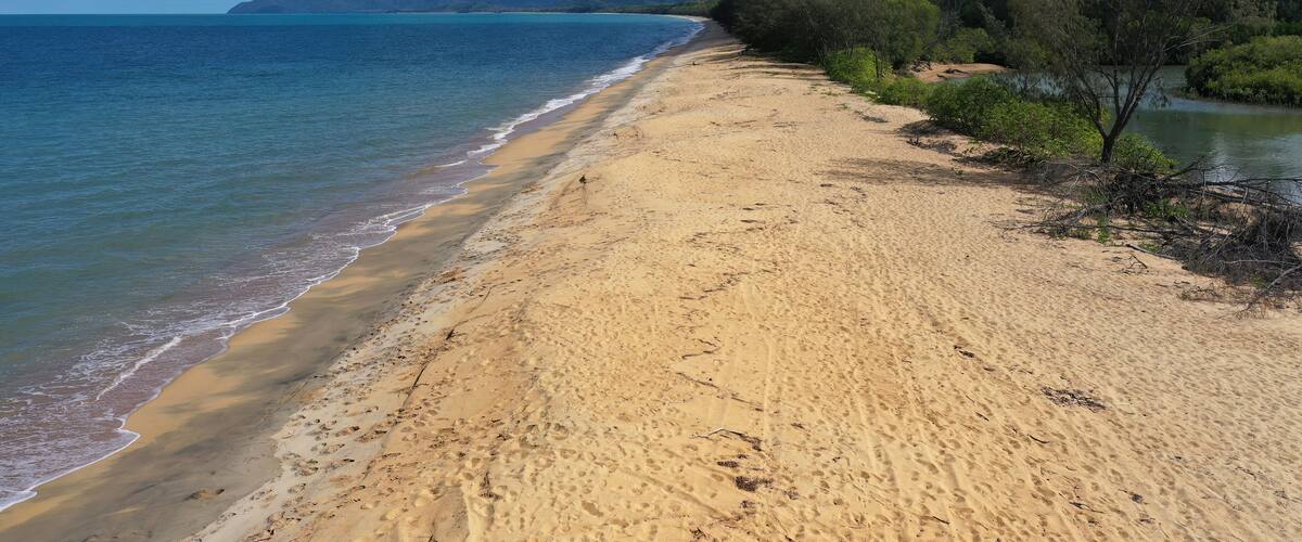 A sandy beach with gentle waves, a clear sky, and distant mountains.