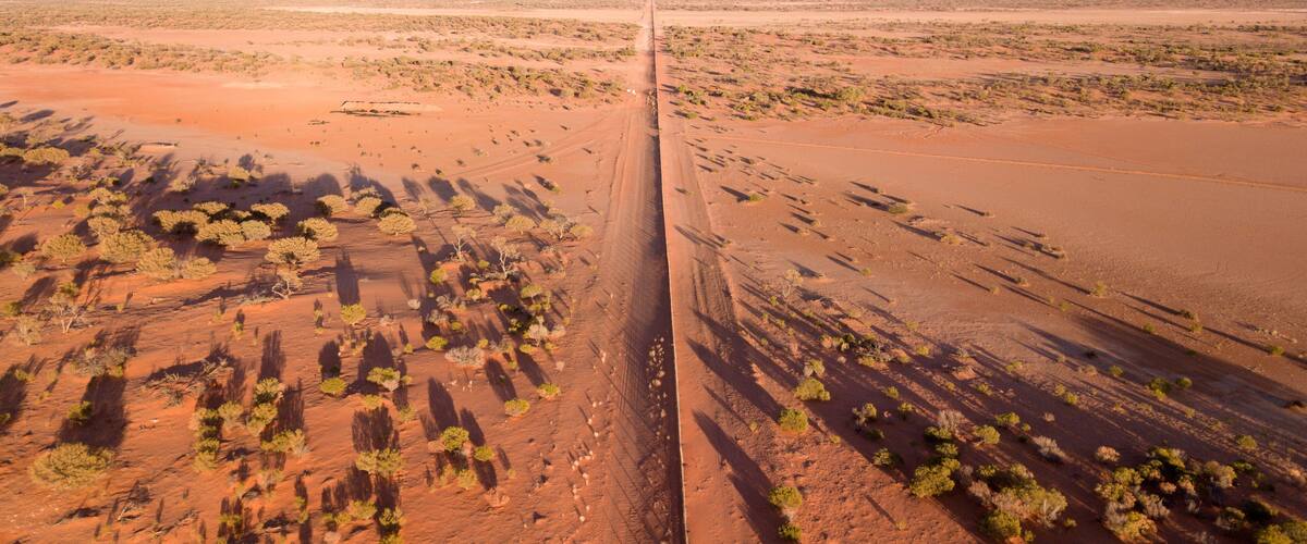 A long, straight road cutting through a desert landscape with sparse vegetation and distant hills.