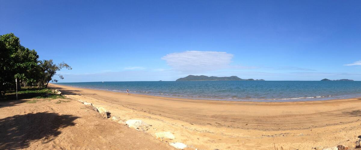 A sandy beach with calm waters, a clear sky, and distant islands.