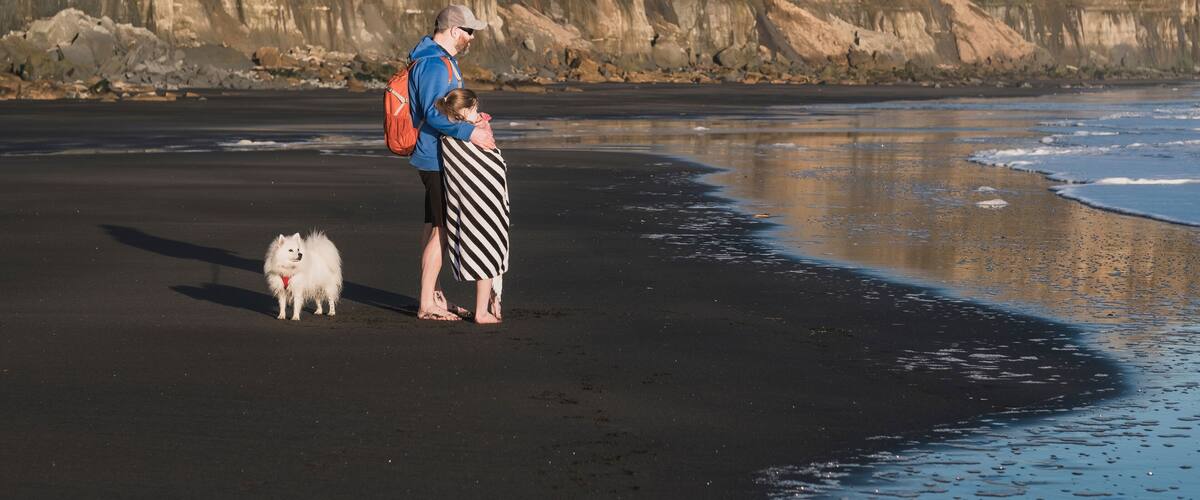 Father holding daughter at the beach with their dog