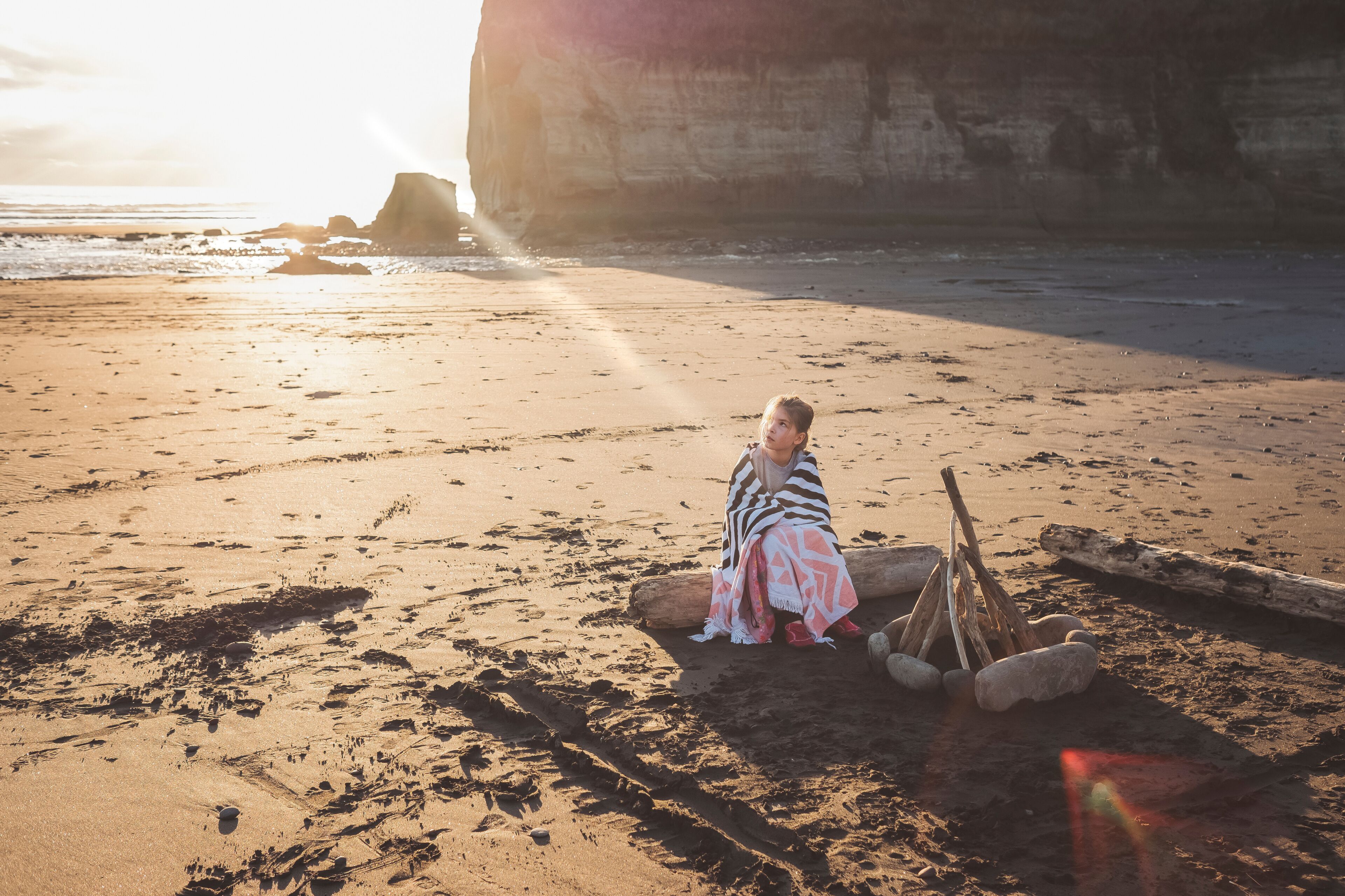 Young girl sitting on driftwood log on the beach