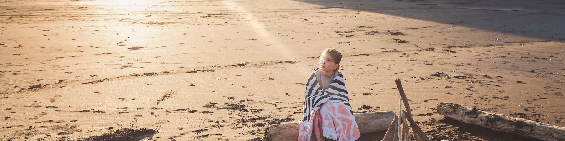 Young girl sitting on driftwood log on the beach