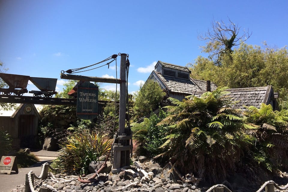 A rustic signpost with 'Traders & Whalers' and a 'Stop' sign, surrounded by lush greenery and a rocky path.
