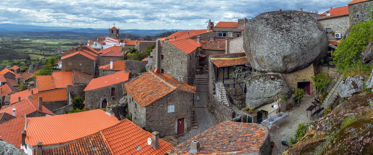 A historic town with red-tiled roofs, stone buildings, and a large rock formation.