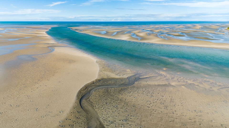A coastal landscape with a wide sandy beach, a clear blue sea, and a narrow water channel.