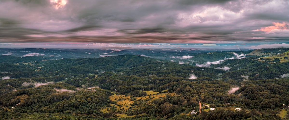 A mountainous landscape with dense forests and a cloudy sky.
