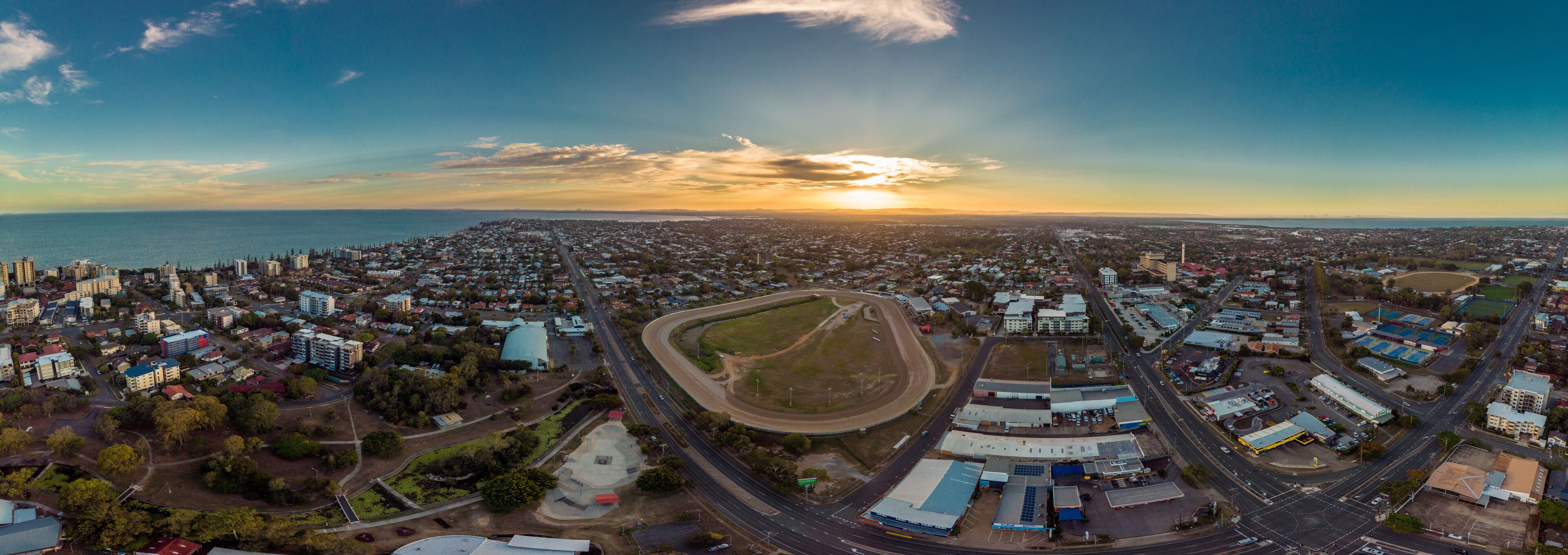 An aerial view of a coastal city at sunset with a prominent highway and industrial area.