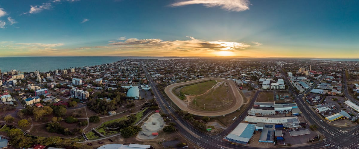 An aerial view of a coastal city at sunset with a prominent highway and industrial area.