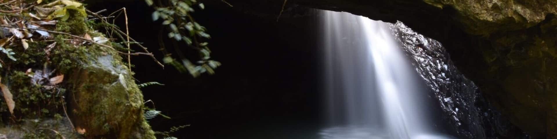 A waterfall flowing through a cave entrance surrounded by moss-covered rocks.