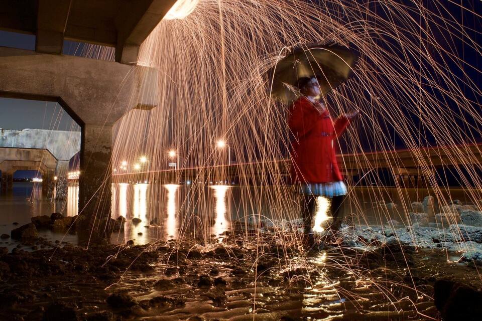 A person under a bridge with sparks flying around.