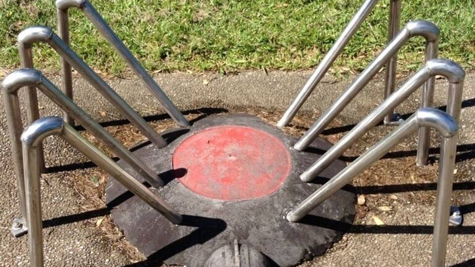 A metal sculpture with a red circular base and a face-like design, surrounded by metal bars.