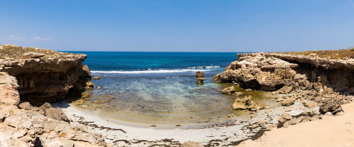A rocky beach with clear blue waters and a sandy center.