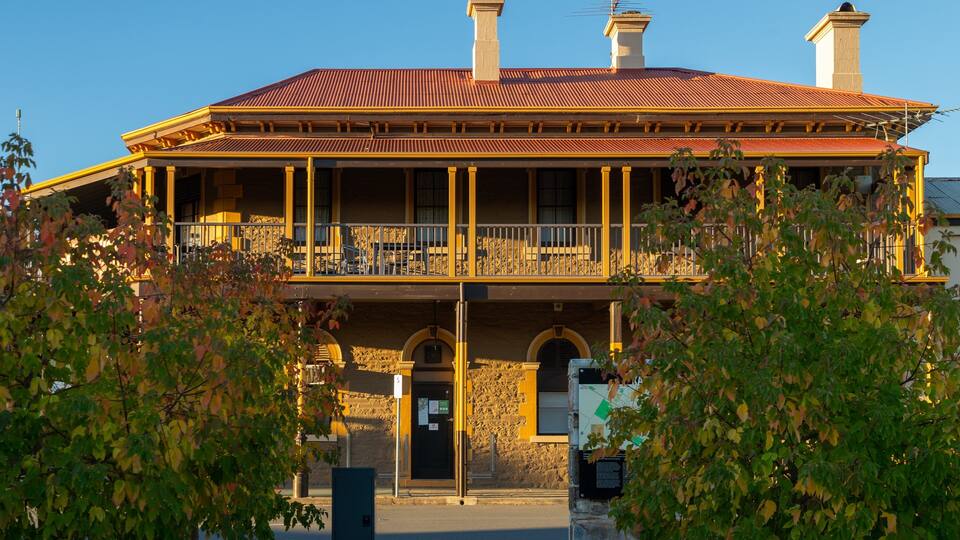 A large two-story building with a red tiled roof, a balcony, and stone walls.