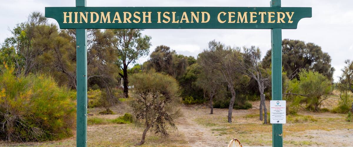 A sign for Hindmarsh Island Cemetery surrounded by sparse vegetation and trees.