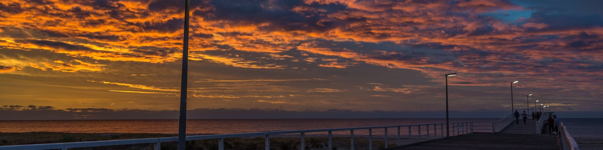 A wooden boardwalk with a railing, leading to a beach with a sunset sky.