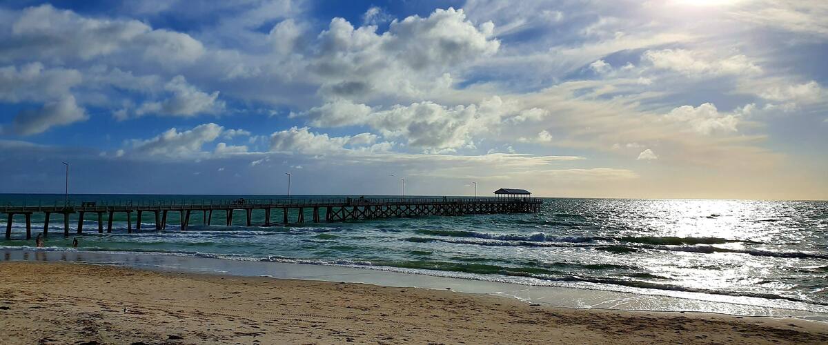 View of a wooden pier at Henley Beach in Australia with a cloudy blue sky in the background