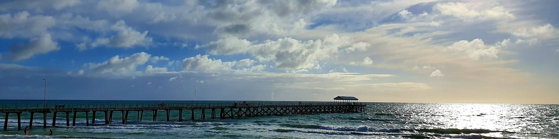 View of a wooden pier at Henley Beach in Australia with a cloudy blue sky in the background