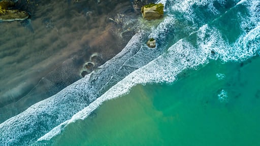 An aerial view of a beach with clear turquoise water, white waves, and rocky outcrops.